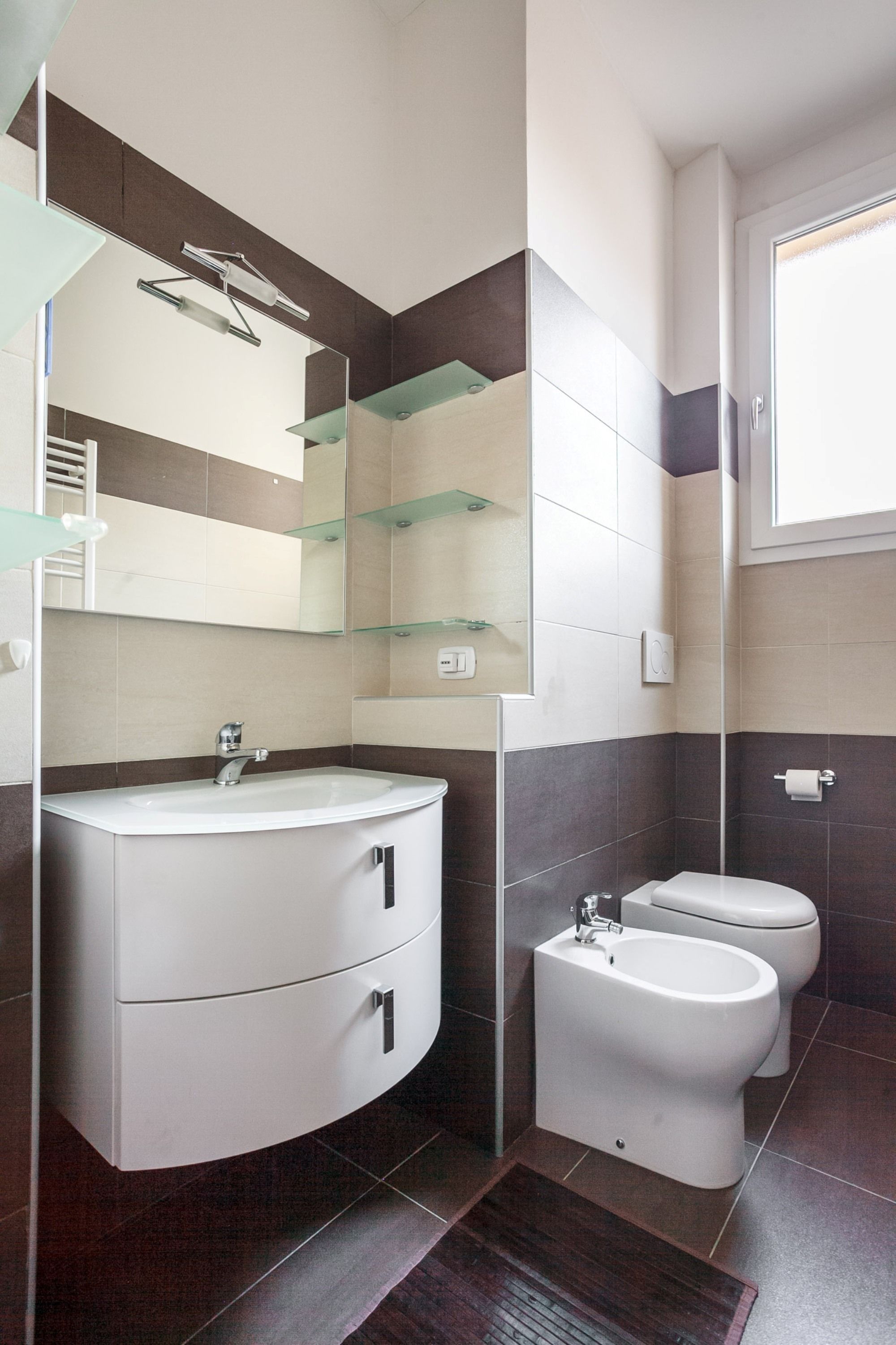 Un baño moderno con un tocador curvo, cabina de ducha de vidrio y un bidé.