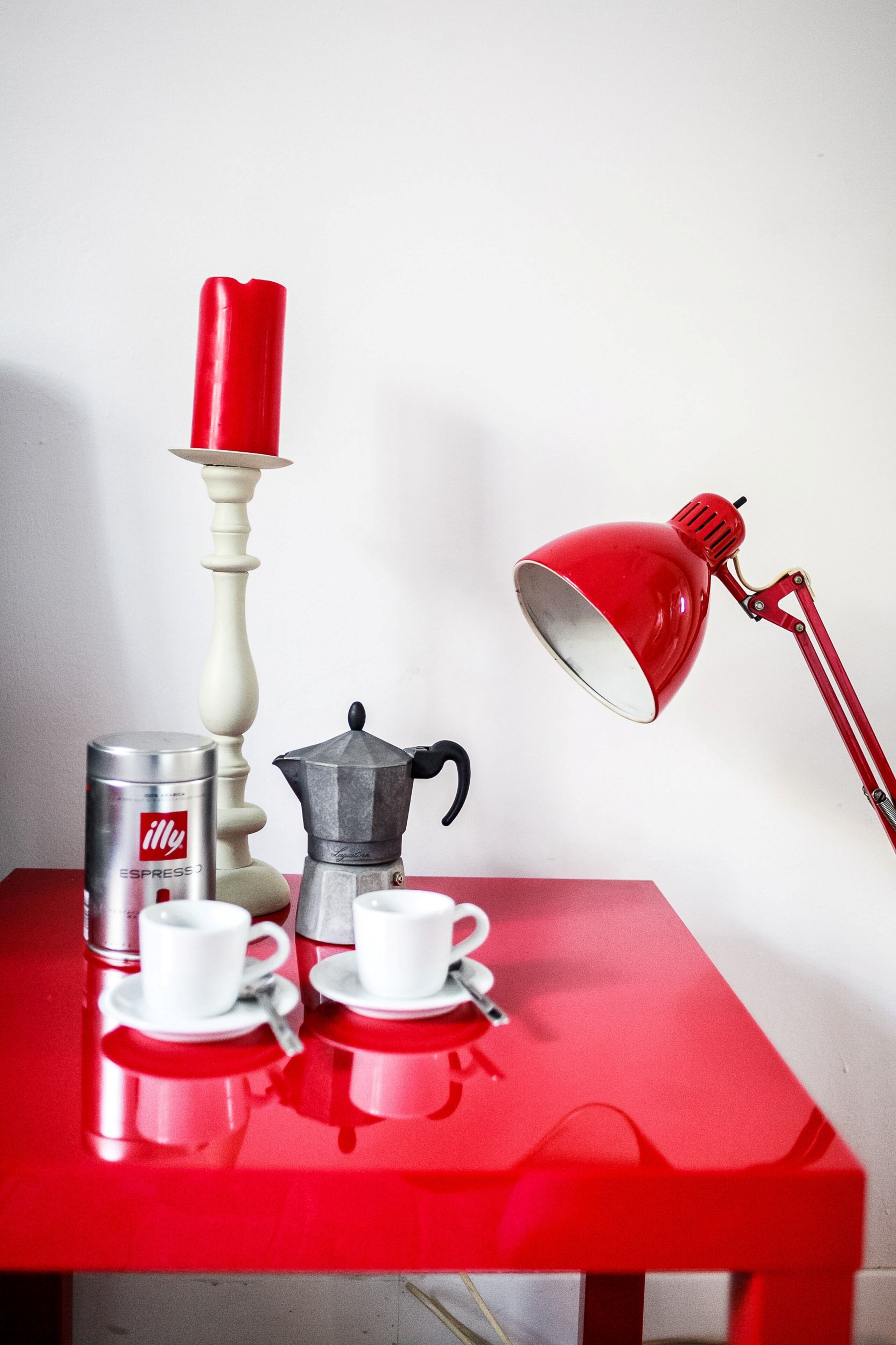 Un tavolo rosso con una macchina per il caffè, una lampada rossa e due tazze bianche su piattini.