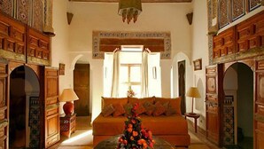 Un interno tradizionale marocchino con un divano, cuscini decorativi, un tavolino da caffè con un vaso di fiori e boiserie in legno finemente lavorata.