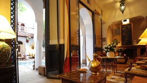 Un interno tradizionale con vista su un'area piscina attraverso un arco, una teiera di ottone su un tavolo e una lampada con base decorata.