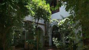 Un cortile interno con archi, piante in vaso e un edificio bianco.