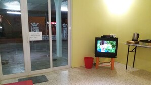 Una habitació amb televisió sobre un suport, un cubet vermell i un cartell a la porta.