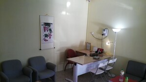 Habitació petita i ben il·luminada amb escriptori, dues cadires, taula petita i làmpada penjada a la paret.