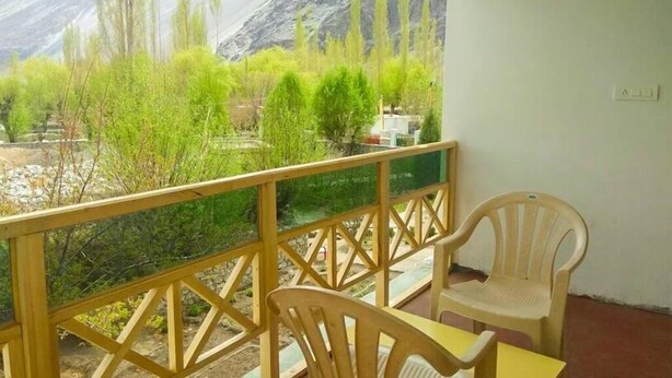 A balcony with a wooden railing, a plastic chair, and a table. - Galaxy Guest House (Leh)