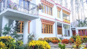 A multi-story building with white walls and red accents, featuring balconies with metal railings and flower pots. - Galaxy Guest House (Leh)