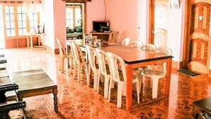 A dining area with a long table and chairs, a television, and a door with a decorative panel. - Galaxy Guest House (Leh)