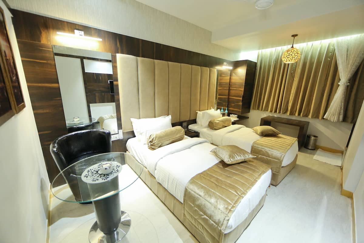 A hotel room with two beds, a large mirror, a glass table with a candle, and a curtain with a unique pattern.
