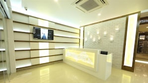 Un área de recepción de diseño moderno, que incluye un mostrador de recepción, un televisor montado y una pared con diseño de ladrillo.