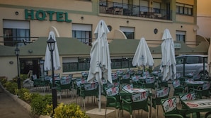 A hotel with outdoor seating area, green chairs, white umbrellas, and a sign reading "HOTEL". - Hotel Brisamar (Gozon)