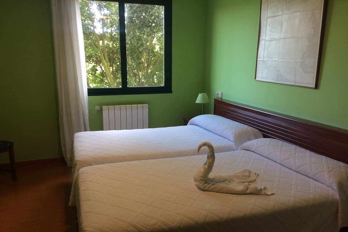 Una habitación con dos camas, una ventana que da a árboles, un radiador y una lámpara.