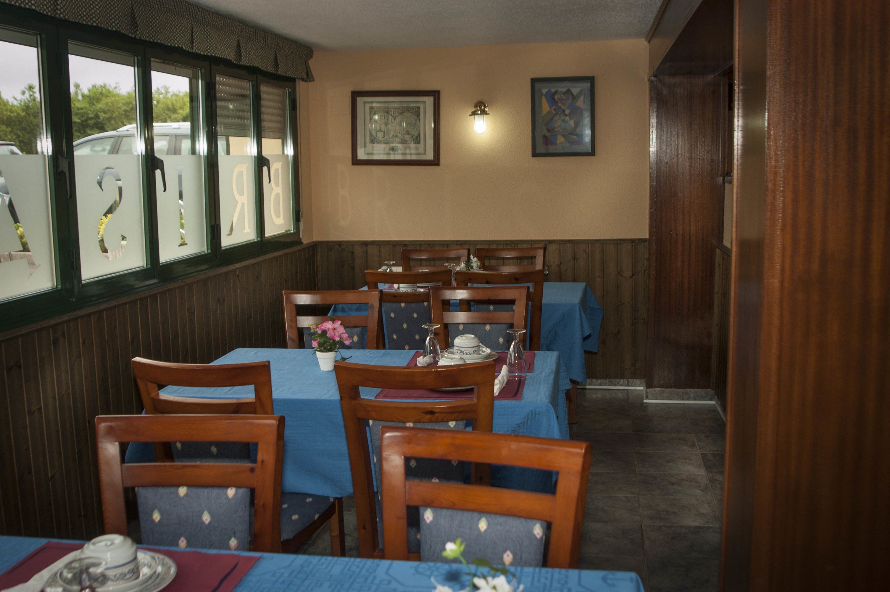 A restaurant with wooden chairs and tables, framed artwork on the wall, and a window with frosted glass.
