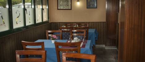 A restaurant with wooden chairs and tables, framed artwork on the wall, and a window with frosted glass.