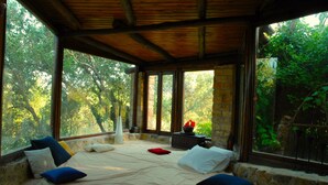 A room with a large bed, stone walls, and large windows offering a view of trees. - Elia Traditional Hotel & Spa (Platanias)