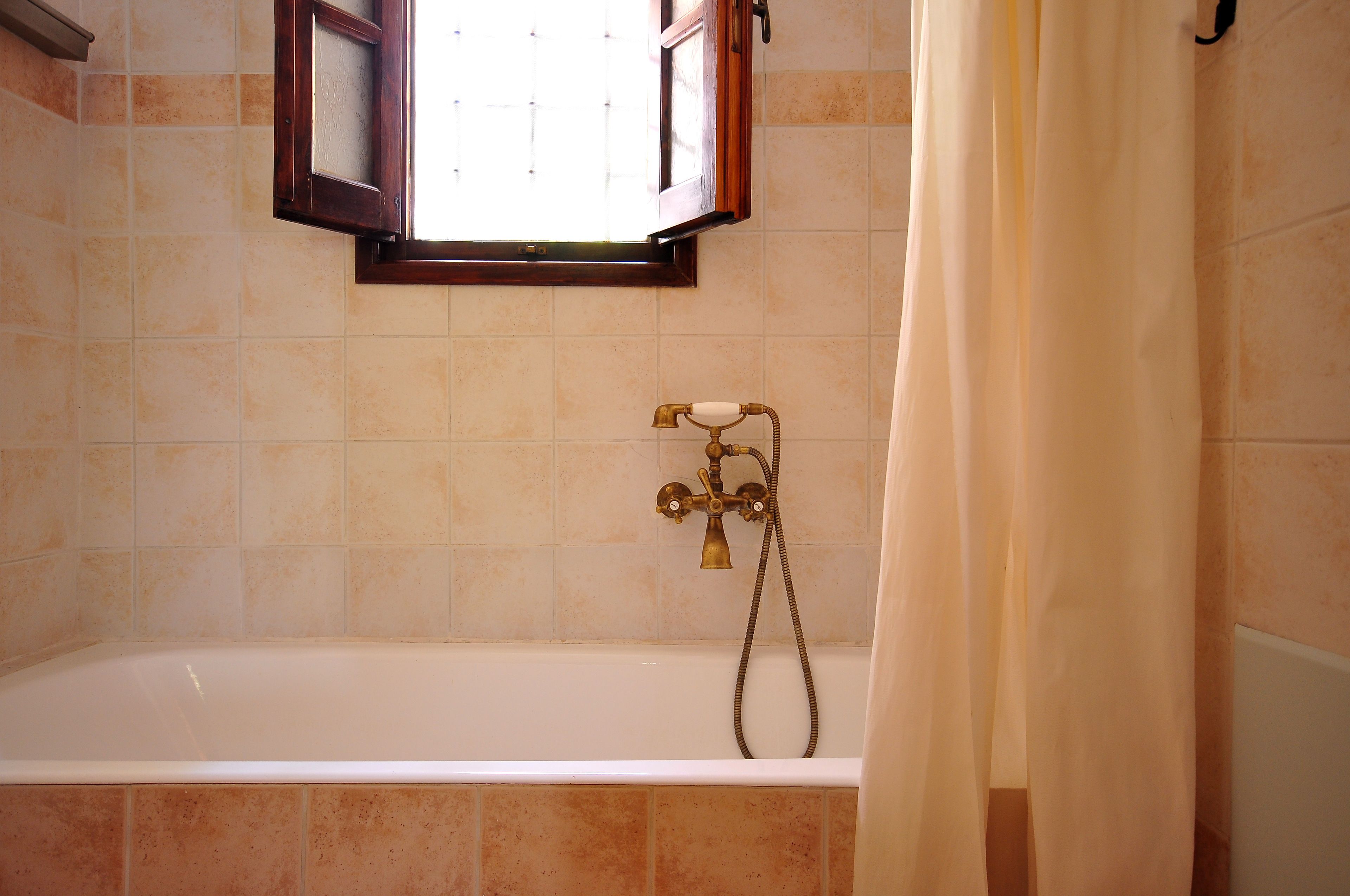 A bathroom with a bathtub, a window with an open wooden shutter, and a shower curtain.