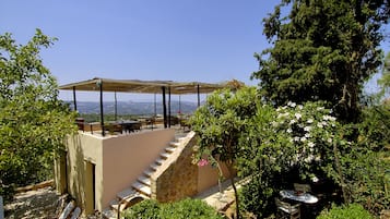 A terrace with a table and chairs, surrounded by greenery and a view of the landscape.