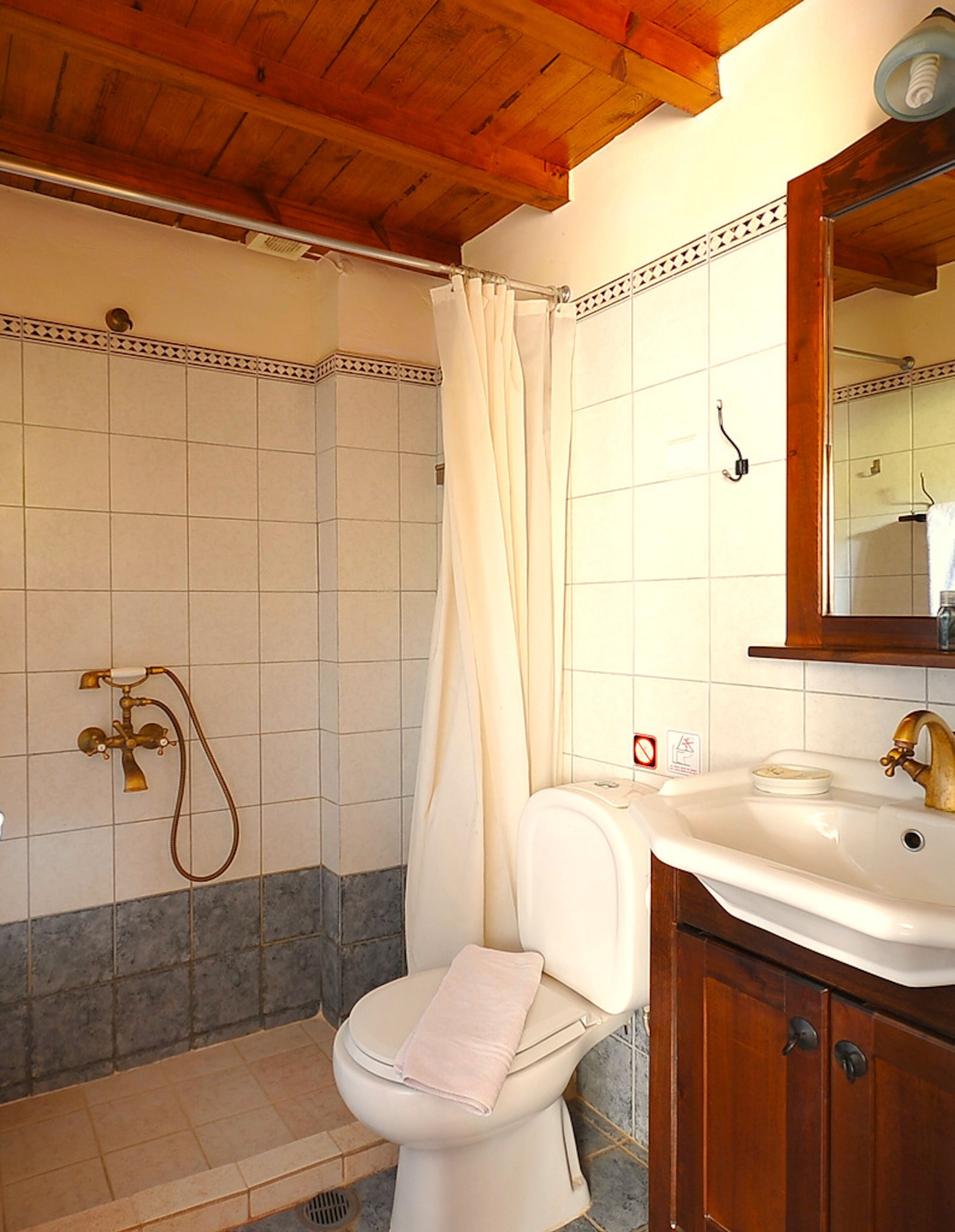 A bathroom with a shower, toilet, sink, and wooden ceiling.