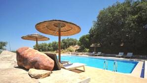 A swimming pool with lounge chairs and umbrellas, surrounded by stone walls and trees. - Elia Traditional Hotel & Spa (Platanias)