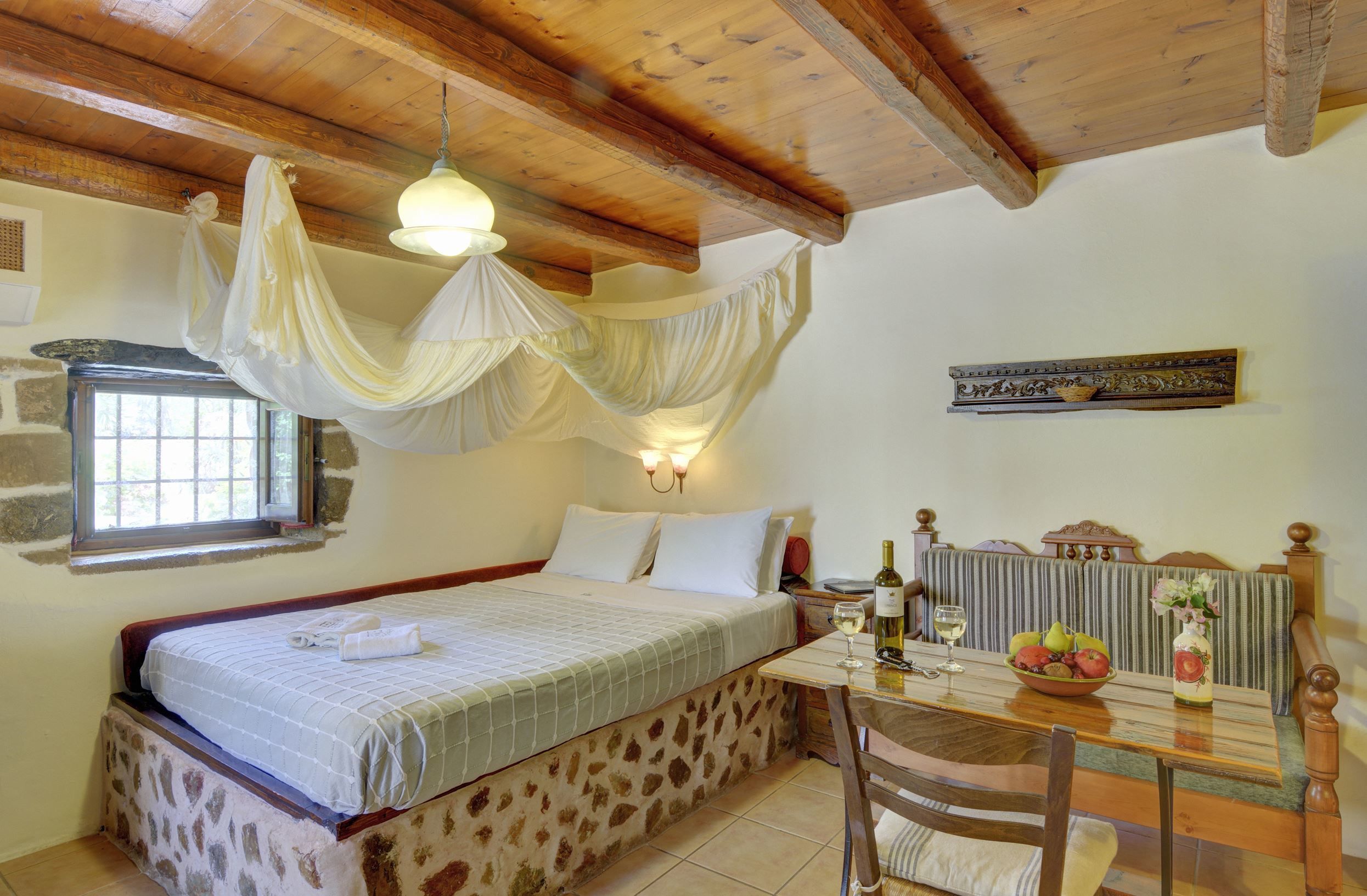 Une chambre à coucher avec un lit, une table sur laquelle se trouvent une bouteille et un verre, et une fenêtre avec des rideaux.