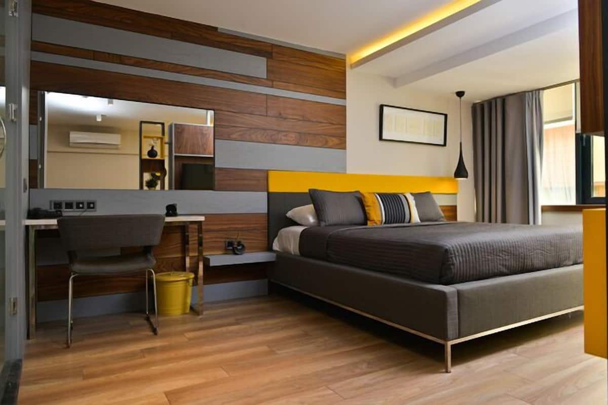 Una habitación de hotel moderna con cama, escritorio, silla y un espejo grande.