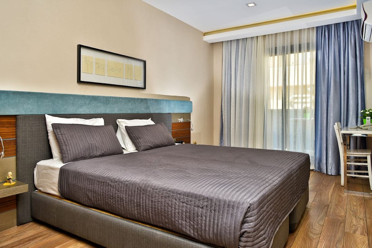 Una habitación de hotel con una cama grande, un escritorio con silla y un ventanal con cortinas.