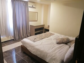 A bedroom with a bed, a wooden nightstand, a mirror, and a window with curtains.