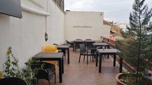 An outdoor patio with tables and chairs, potted plants, and a wall with Arabic text. - Milano Hotel Suites (Amman)