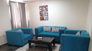 A living room with a blue sofa set, a coffee table, and a patterned painting on the wall. - Milano Hotel Suites (Amman)