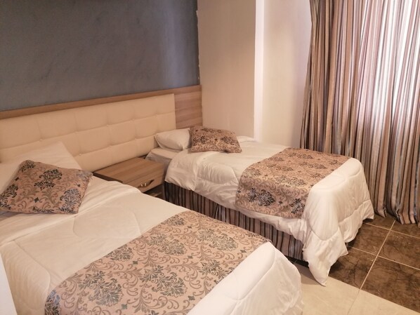 A hotel room with two beds, each with patterned bedding and a wooden nightstand.