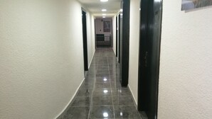 A corridor with tiled flooring and white walls, leading to a door with a number plate. - Milano Hotel Suites (Amman)