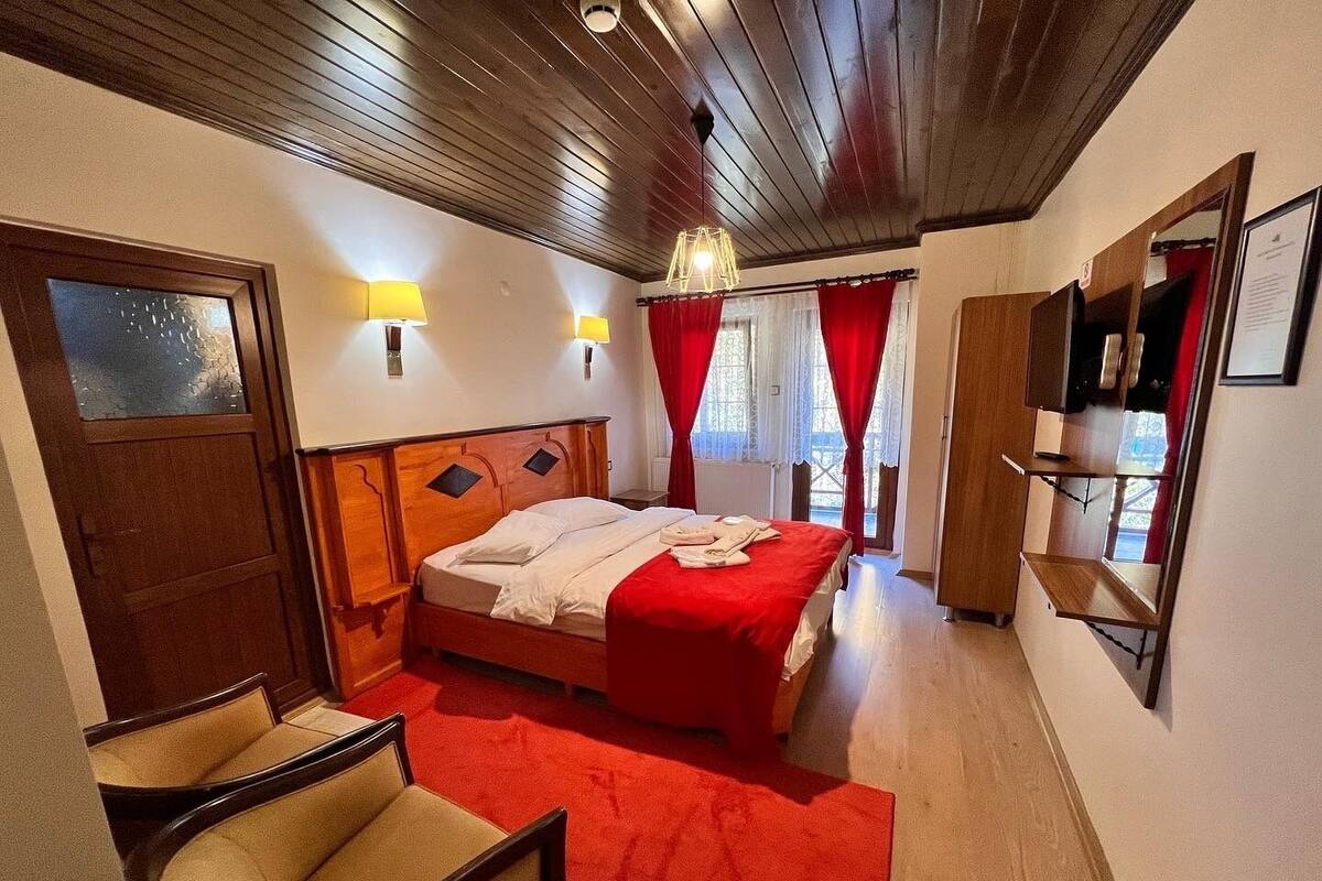 Ein Hotelzimmer mit Holzboden, einem Bett mit roter Bettdecke, einem Sessel und einem Schreibtisch mit Spiegel.