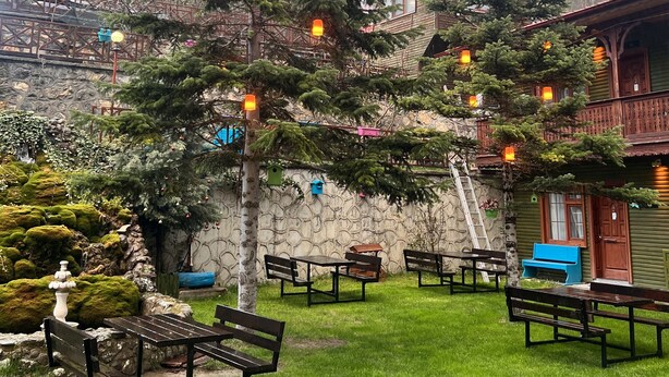 A rustic lodge with wooden cabins, a stone wall, and a well-maintained garden with benches and a large tree. - Abant Dort Mevsim Konagi (Bolu)
