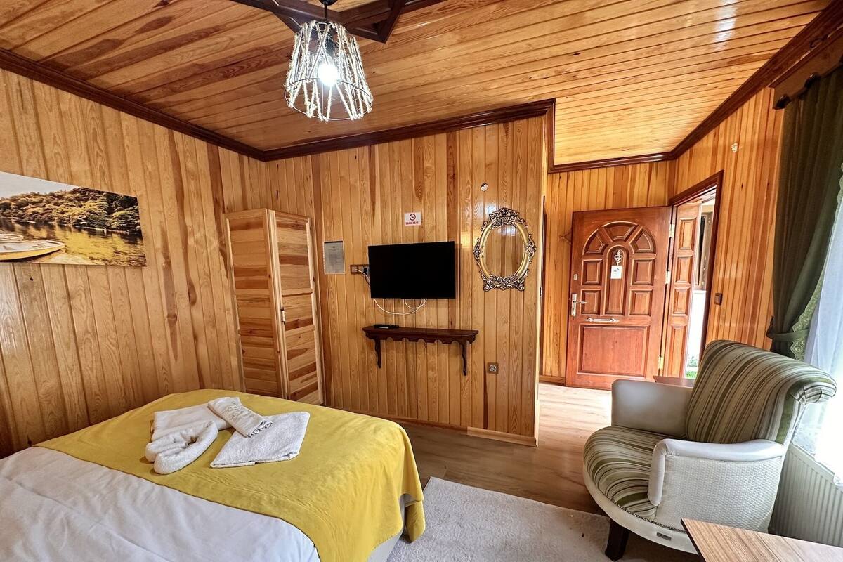Ein Zimmer mit Holzwandverkleidung, einem Bett, einem Sessel, einem Fernseher und einer Tür.