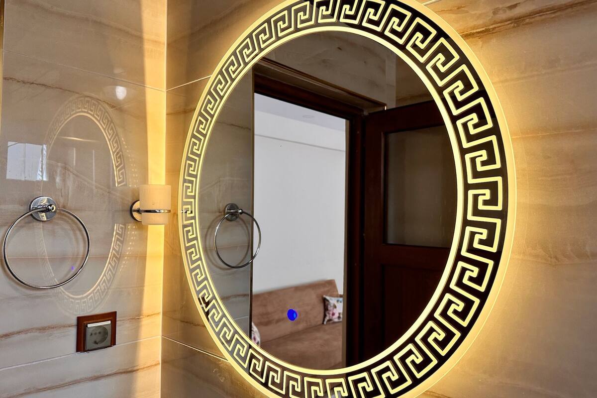Ein Badezimmer mit einem großen Spiegel mit dekorativem Schwarz-Gold-Rahmen, zwei Handtuchringen und einer Holztür.