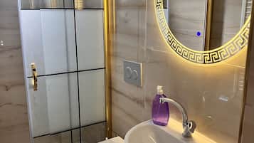 A modern bathroom with a glass-enclosed shower, a white toilet, and a pedestal sink with a mirror.