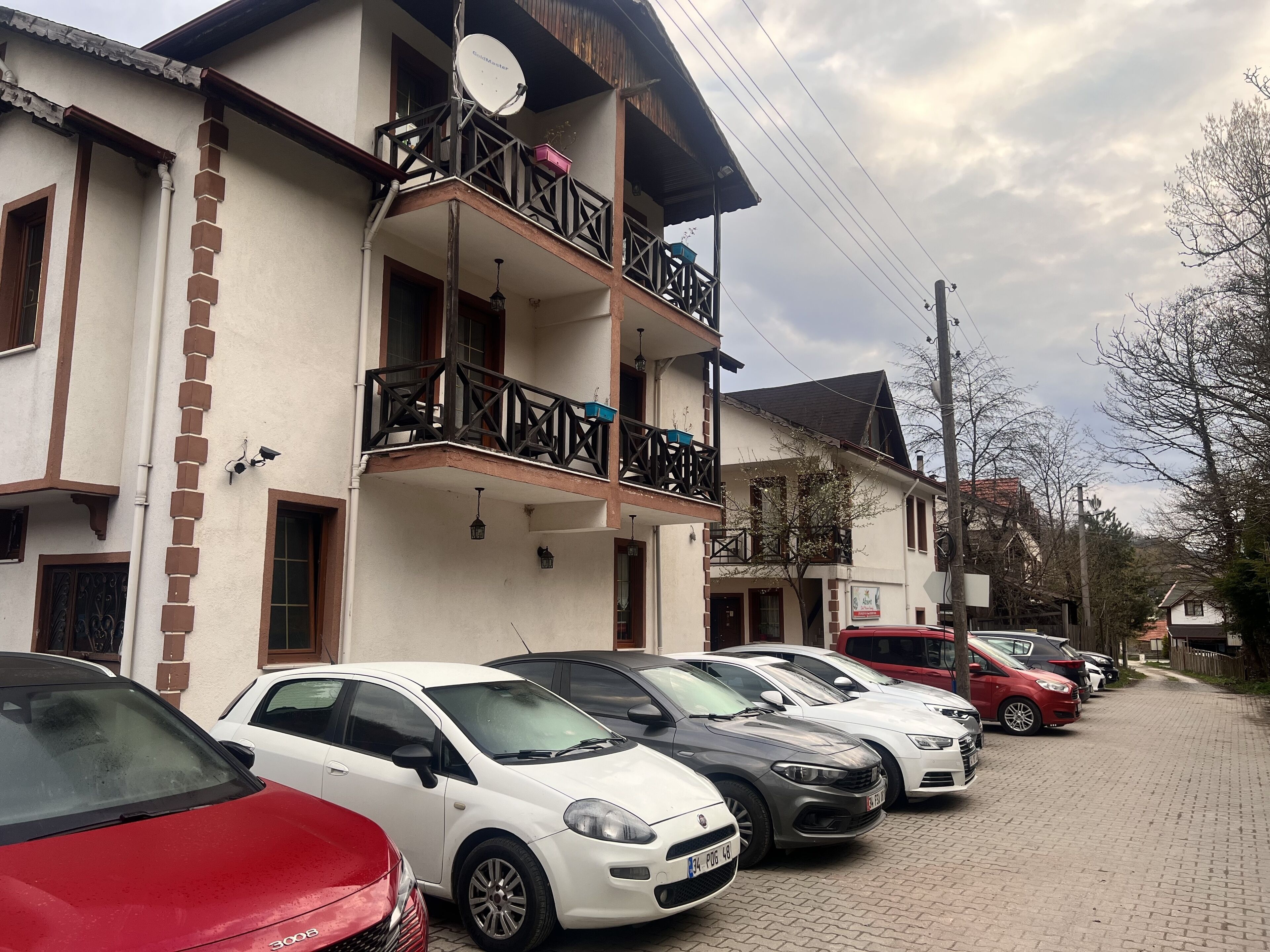 Une rangée de voitures garées le long d’une rue pavée, devant un immeuble doté d’un balcon et d’une antenne parabolique.