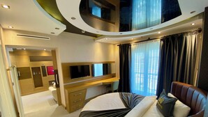 A modern hotel room with a curved ceiling, a bed with a black and white bedspread, a leather sofa, a TV mounted on the wall, and a large window with curtains. - Grand Hotel Van (Van)