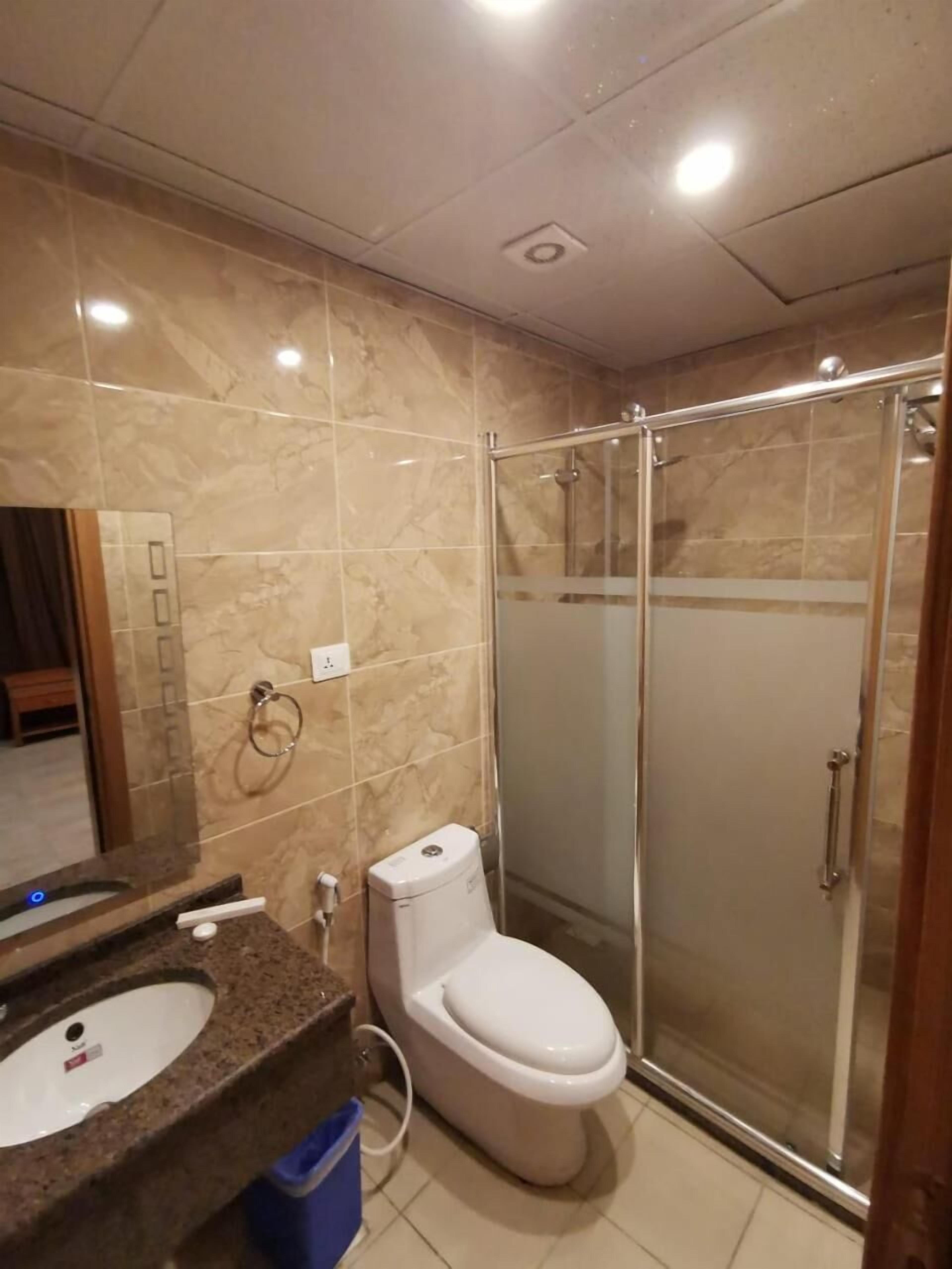A bathroom with a marble floor, a sink, a toilet, and a glass-enclosed shower.