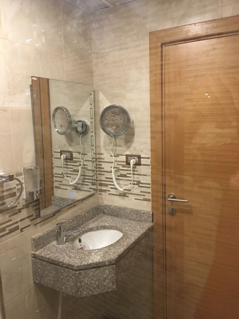 Une salle de bain avec un lavabo en granit, deux miroirs, une porte en bois et un mur carrelé.
