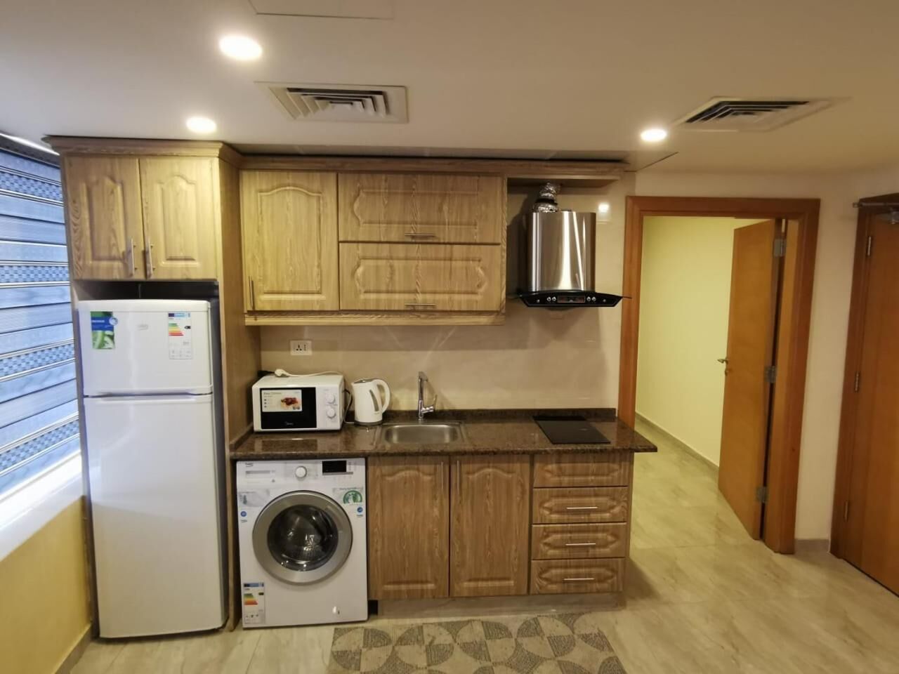 A compact kitchen with wooden cabinets, a built-in washing machine, a microwave, and a stainless steel range hood.