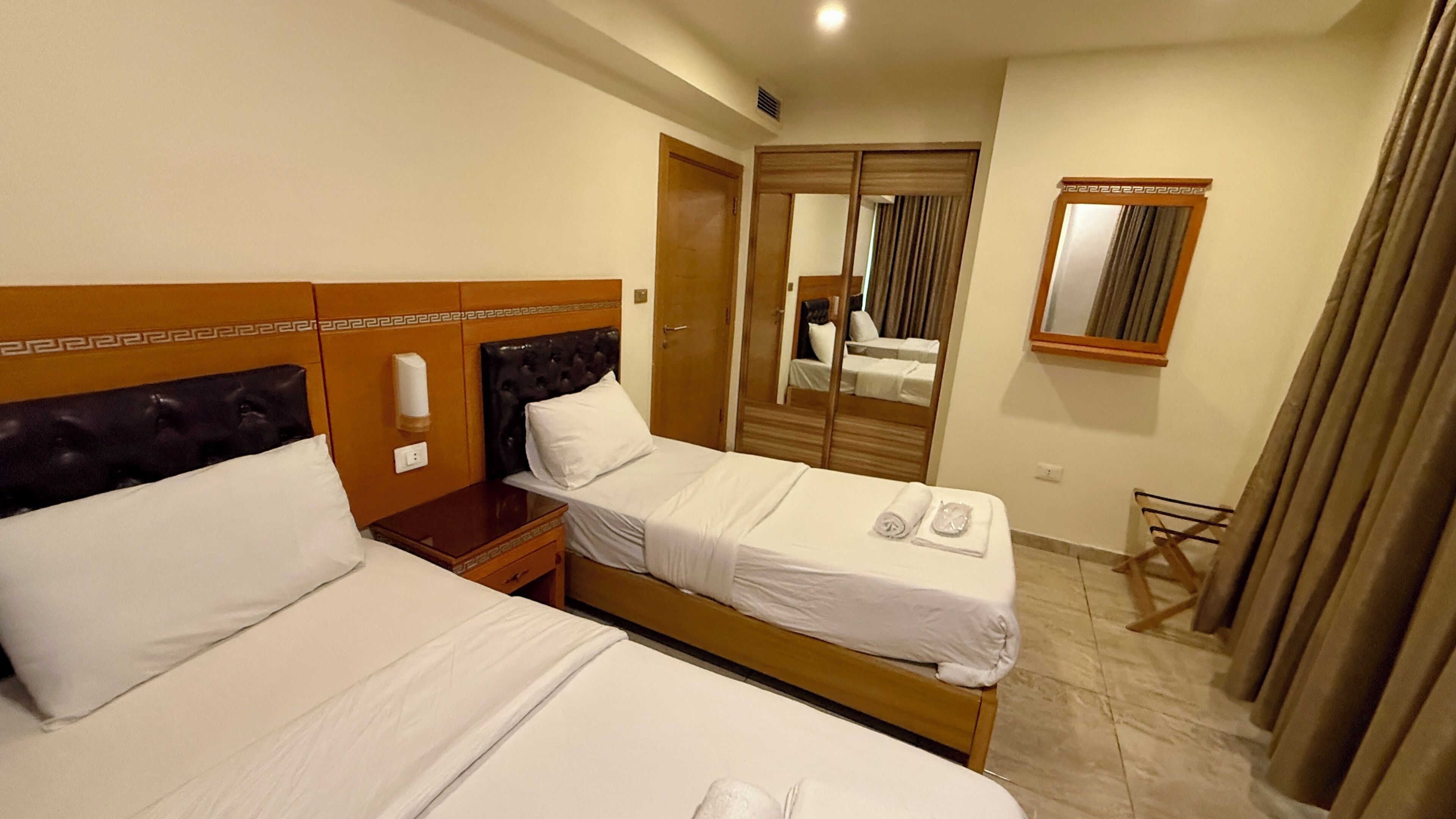 A hotel room with two beds, a wooden headboard, a nightstand, a mirror, and a small chair.
