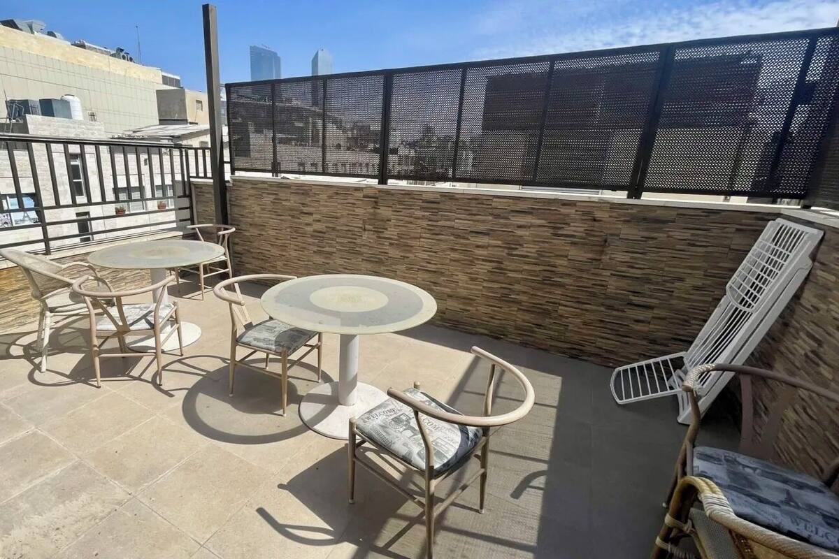 Eine Dachterrasse mit rundem Tisch und Stühlen, einer Metallbank und einem Sichtschutz aus Maschendraht.