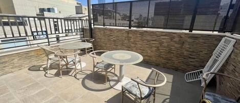 Une terrasse sur le toit avec une table ronde et des chaises, un banc en métal et un paravent en treillis pour plus d'intimité.