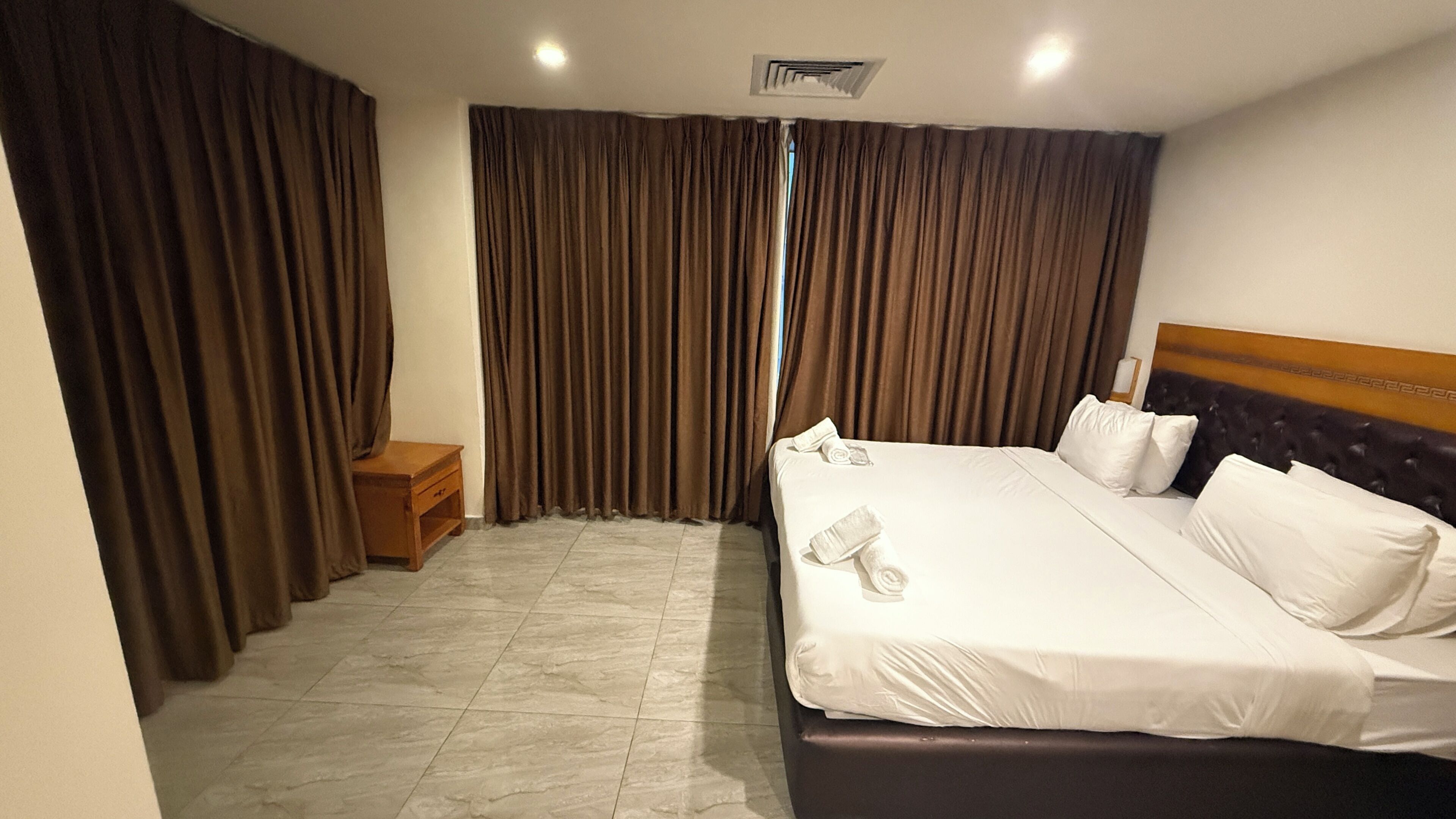 Een hotelkamer met een bed, een nachtkastje en een raam met gordijnen.