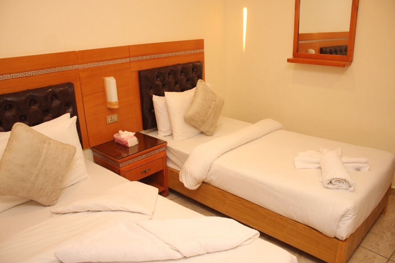 A hotel room with two beds, each with white linens and pillows, a wooden headboard, a nightstand with a lamp, and a mirror on the wall.
