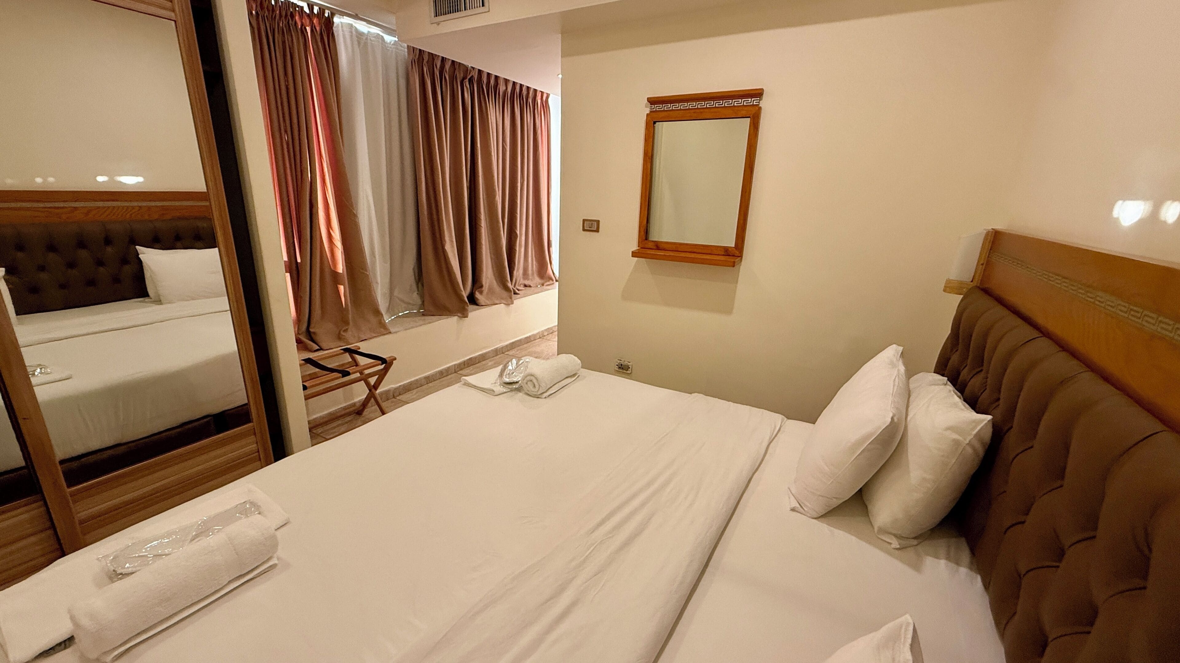 A hotel room with a large bed, a mirror, a headboard, and a window with curtains.