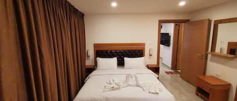 A hotel room with a bed, curtains, a headboard, a nightstand, a bedside table, and a mirror.