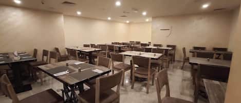 Un comedor amplio con varias mesas y sillas, dispuesto con vajilla y servilletas.