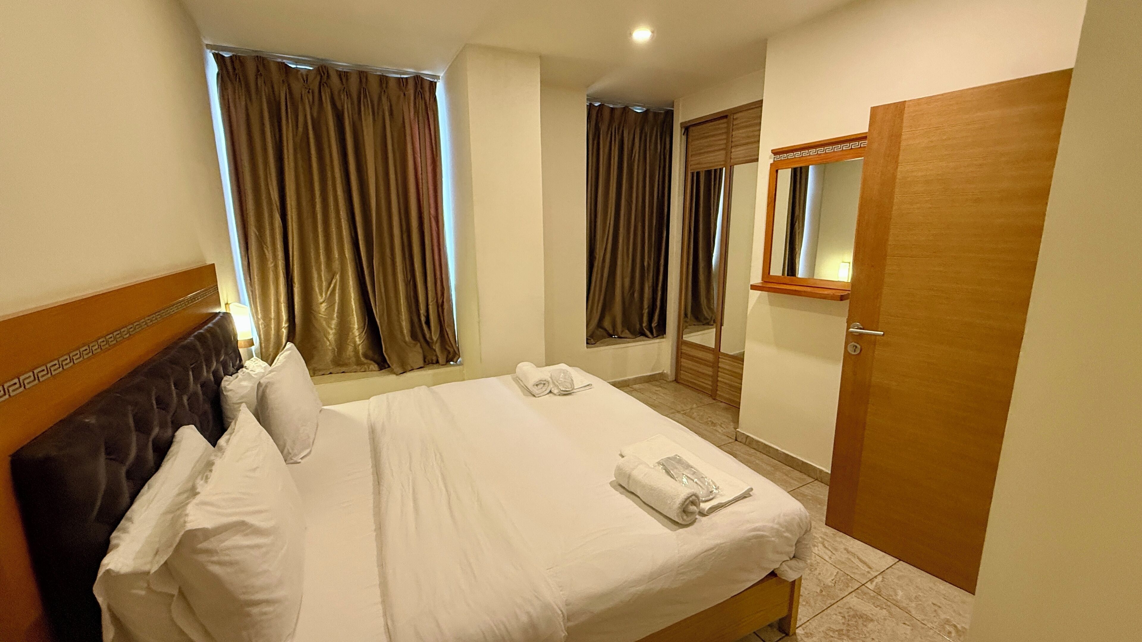 A hotel room with a bed, a mirror, a door, and curtains.