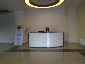 Una reception in un atrio con un grande cartello a sinistra, un lampadario a soffitto e un pavimento piastrellato.