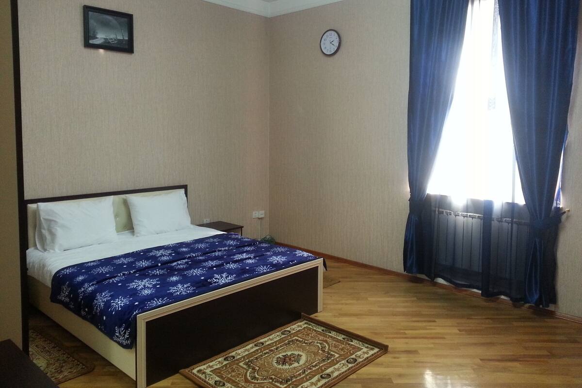 A bedroom with a bed, a clock, and a window with curtains.